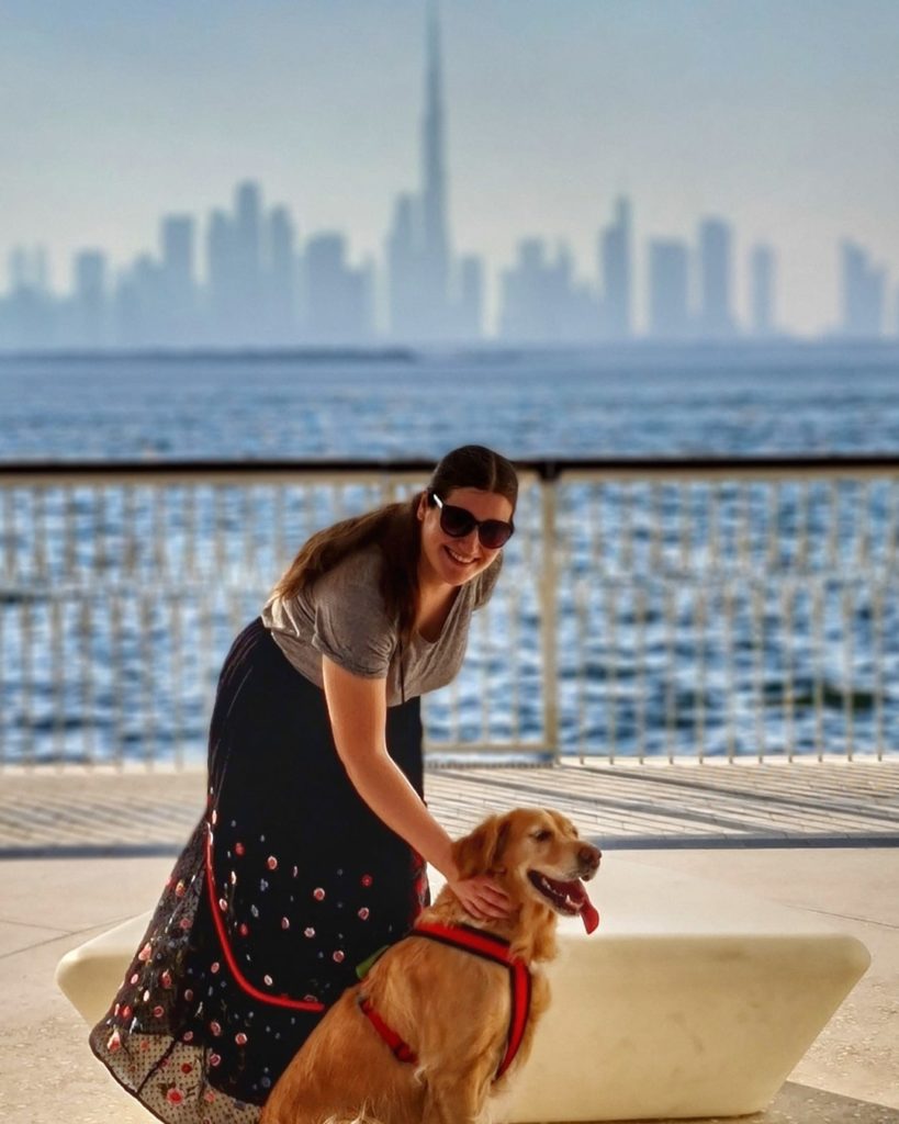 A golden retriever and a woman with the Dubai skyline in the background
